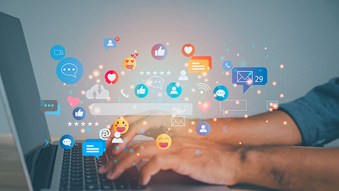 A laptop screen shows a person typing on a keyboard with a variety of social media icons surrounding them.