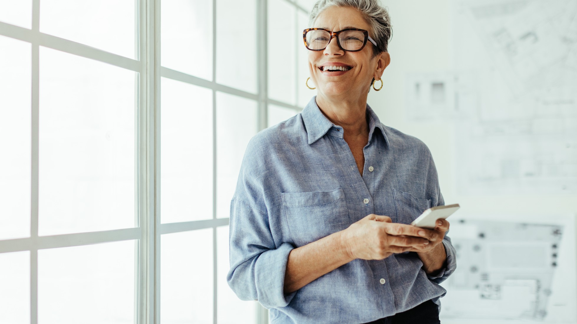 Mature woman smiling and using a mobile phone in her office