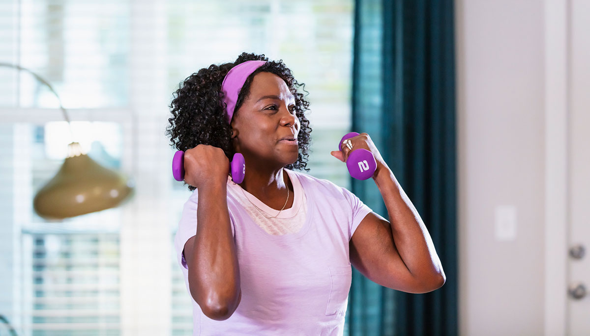 Middle aged black woman using weights at home