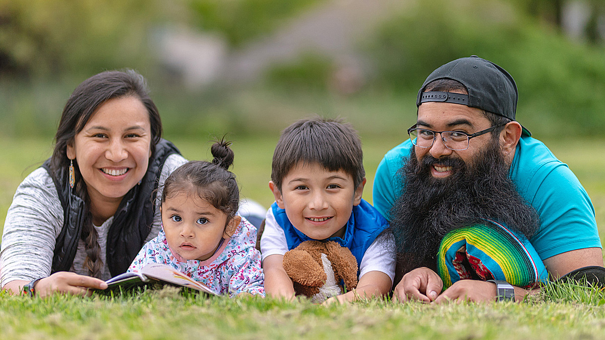 Family Reading in the Park Young, American Indian couple lying in the grass in a park, reading to their two young children.