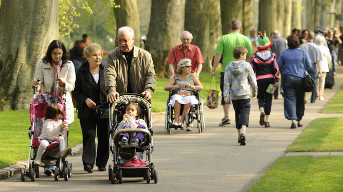 Crowded park of families walking amongst a flower garden.