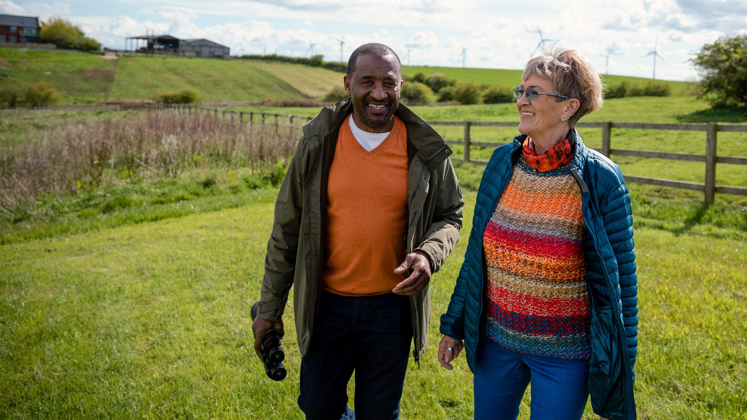 -- title missing -- Two people walking and talking in a field in a rural setting.