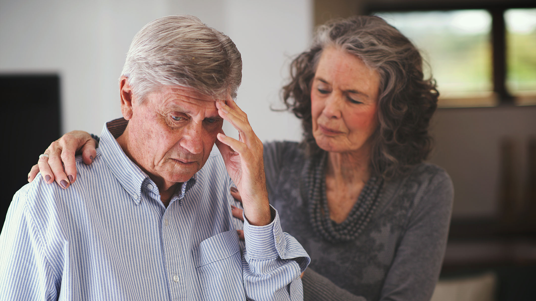 A woman comforts a man who is holding his head.