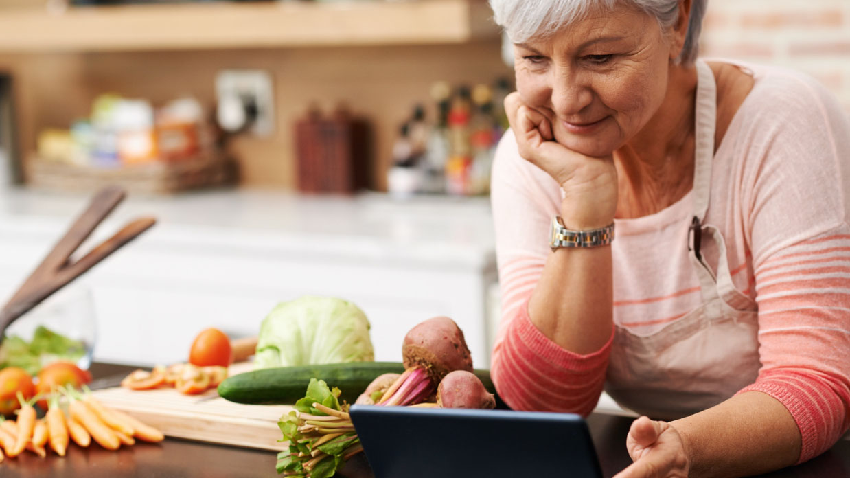 A woman reading a recipe while preparing vegetables A woman reading recipe on tablet while preparing vegetables.